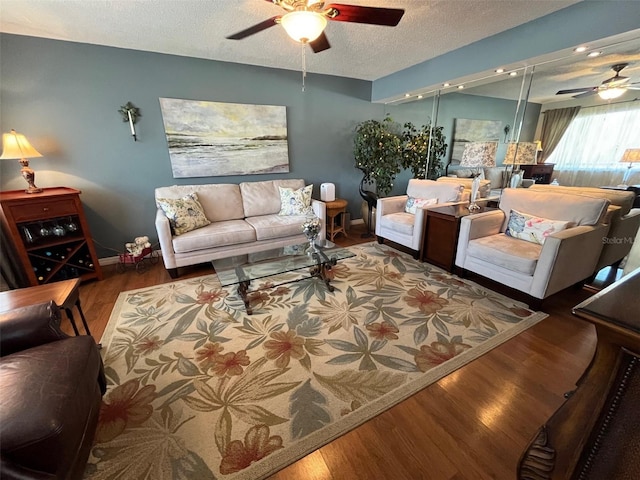 living area with ceiling fan, a textured ceiling, baseboards, and wood finished floors