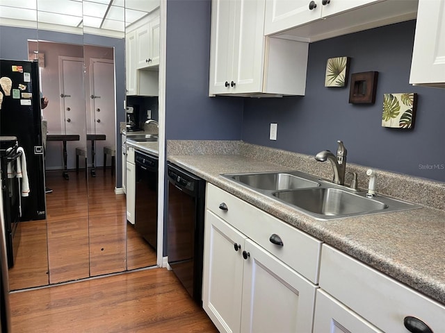 kitchen featuring a paneled ceiling, wood finished floors, a sink, white cabinets, and black appliances