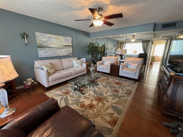 living room featuring visible vents, a ceiling fan, a textured ceiling, wood finished floors, and baseboards