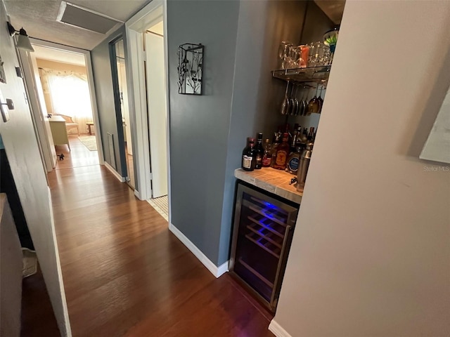 bar featuring a bar, beverage cooler, baseboards, and wood finished floors