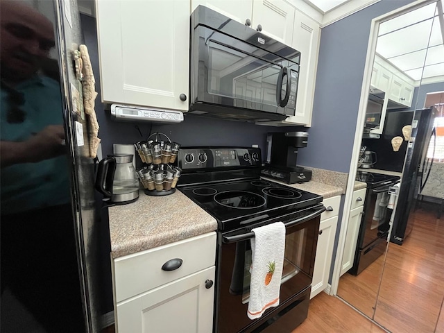 kitchen with black appliances, light countertops, light wood-style flooring, and white cabinetry