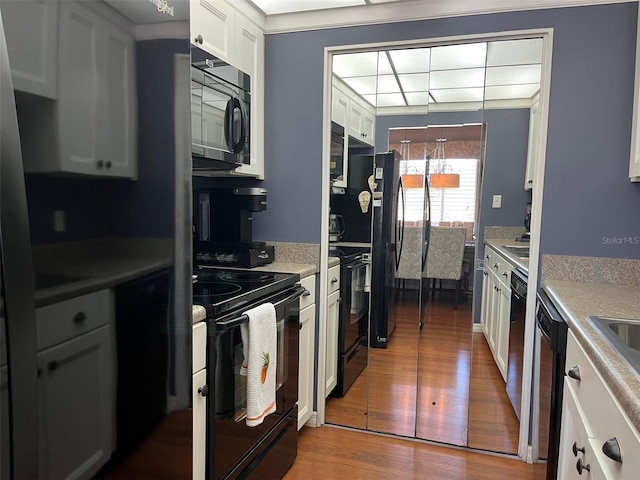 kitchen with black appliances, white cabinetry, light countertops, and wood finished floors