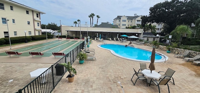 community pool featuring shuffleboard, fence, and a patio