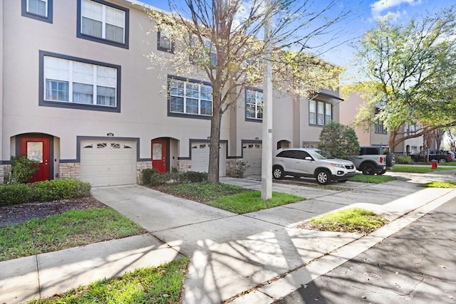 townhome / multi-family property with driveway, stone siding, a garage, and stucco siding