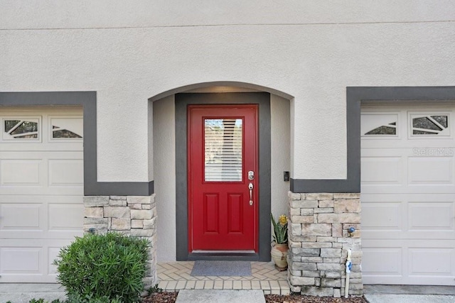 doorway to property with a garage, stone siding, and stucco siding