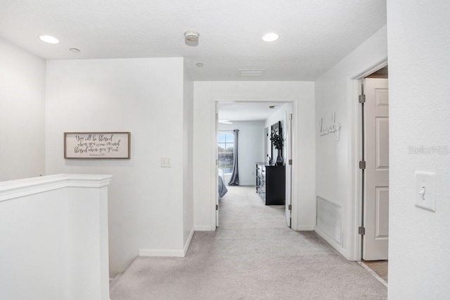 corridor with recessed lighting, light colored carpet, visible vents, a textured ceiling, and baseboards