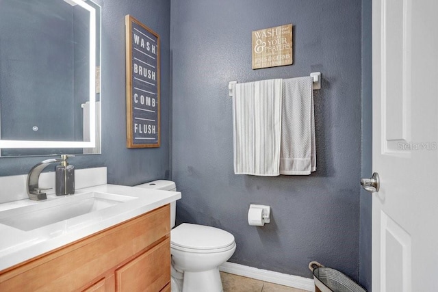 half bath with toilet, vanity, baseboards, and tile patterned floors