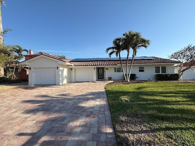 view of front of property featuring a garage, roof mounted solar panels, a front lawn, and decorative driveway