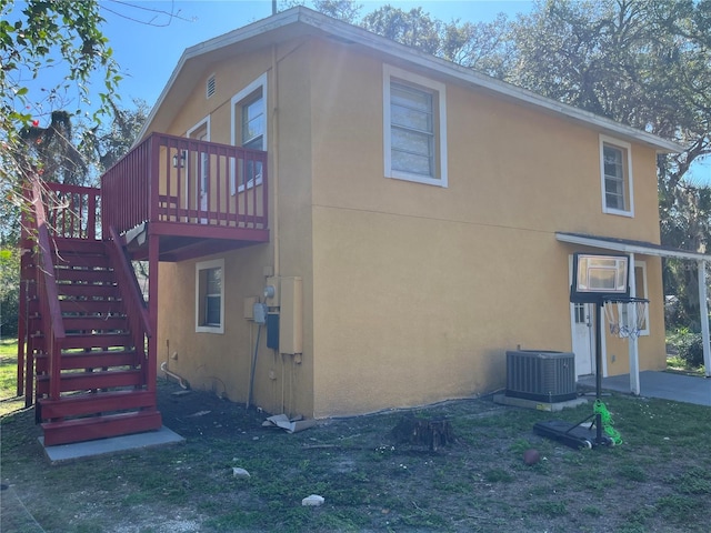 view of side of property with stairs, central AC unit, a deck, and stucco siding