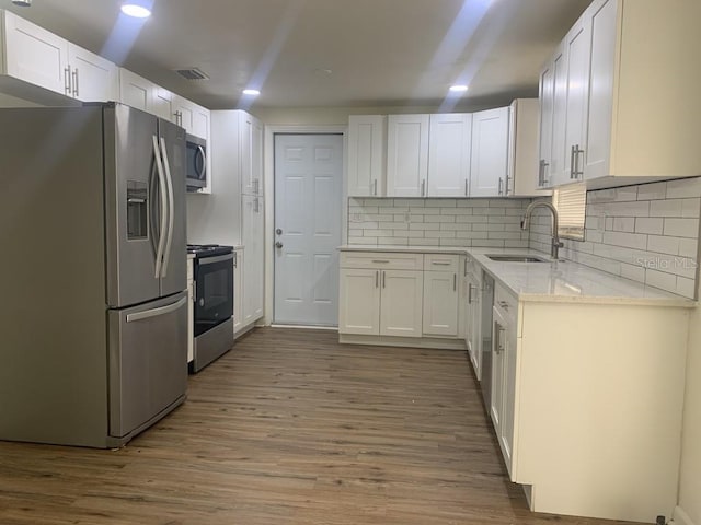 kitchen featuring visible vents, appliances with stainless steel finishes, white cabinetry, a sink, and wood finished floors