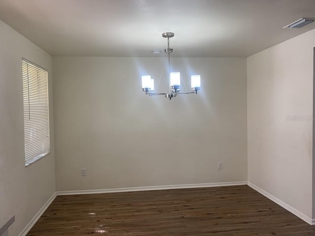 empty room with baseboards, dark wood-type flooring, visible vents, and a notable chandelier