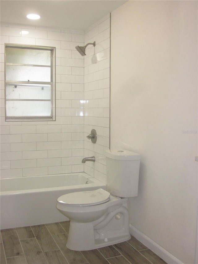 bathroom with toilet, baseboards,  shower combination, and wood finish floors