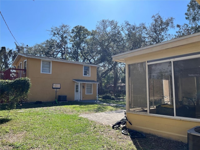 back of house with a sunroom, stucco siding, cooling unit, and a yard