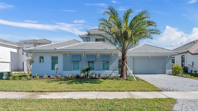 view of front of property featuring a garage, a tiled roof, decorative driveway, a front lawn, and stucco siding