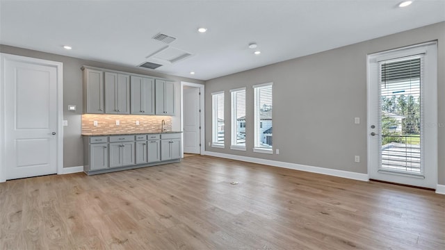 kitchen featuring plenty of natural light, gray cabinets, light wood-style flooring, and decorative backsplash