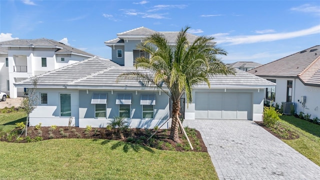 view of front facade with decorative driveway, stucco siding, a garage, cooling unit, and a front lawn