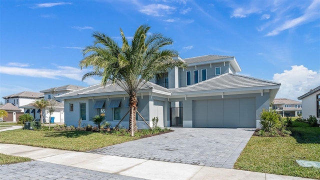 view of front facade with a tiled roof, an attached garage, decorative driveway, a front lawn, and stucco siding