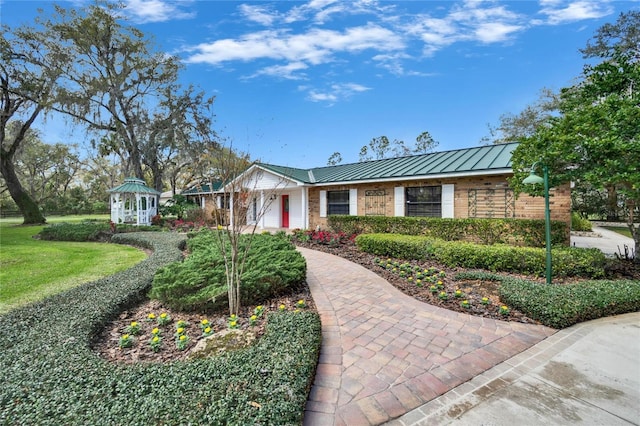 ranch-style house with metal roof, an attached garage, a standing seam roof, a gazebo, and brick siding