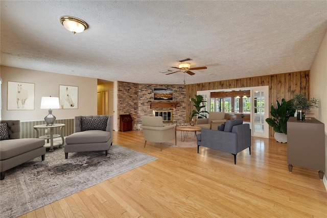 living room featuring a fireplace, visible vents, light wood-style flooring, wood walls, and a textured ceiling