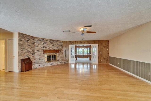 unfurnished living room featuring visible vents, ceiling fan, wood finished floors, a textured ceiling, and a brick fireplace