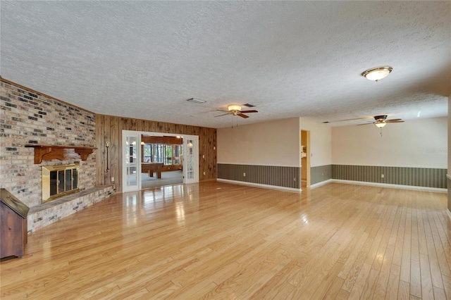 unfurnished living room featuring ceiling fan, a textured ceiling, hardwood / wood-style flooring, visible vents, and a brick fireplace