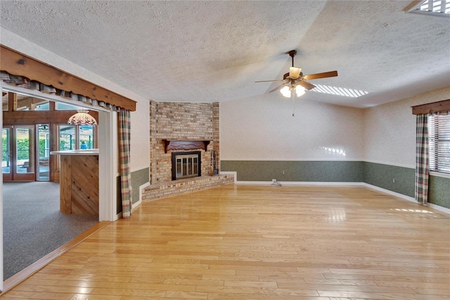 unfurnished living room with a wainscoted wall, a brick fireplace, vaulted ceiling, a textured ceiling, and hardwood / wood-style flooring