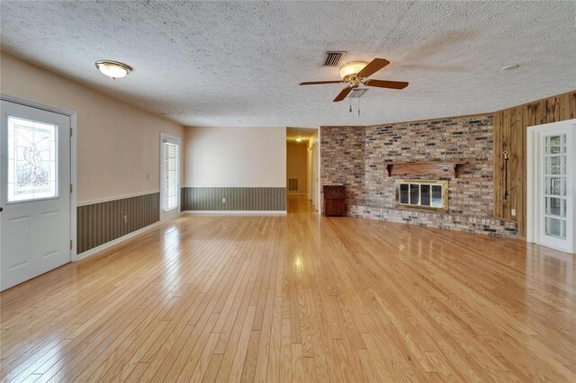 unfurnished living room featuring a textured ceiling, a fireplace, hardwood / wood-style floors, and wainscoting