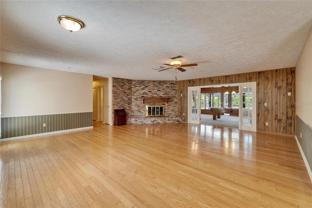 unfurnished living room featuring visible vents, a brick fireplace, ceiling fan, a textured ceiling, and wood finished floors