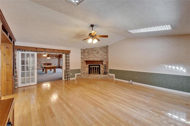 unfurnished living room featuring a textured ceiling, hardwood / wood-style flooring, a fireplace, a ceiling fan, and vaulted ceiling