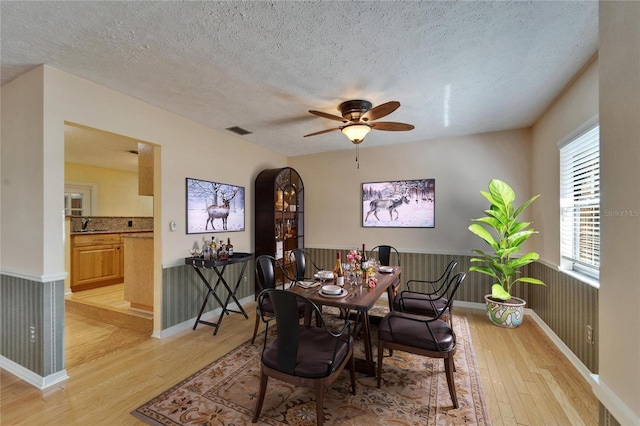 dining space featuring a textured ceiling, ceiling fan, light wood-style flooring, and visible vents