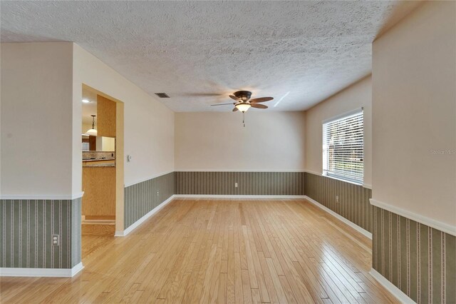 unfurnished room with a textured ceiling, hardwood / wood-style floors, wainscoting, and visible vents