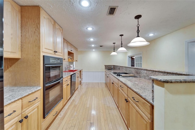 kitchen featuring dobule oven black, visible vents, a wainscoted wall, light brown cabinetry, and stainless steel dishwasher