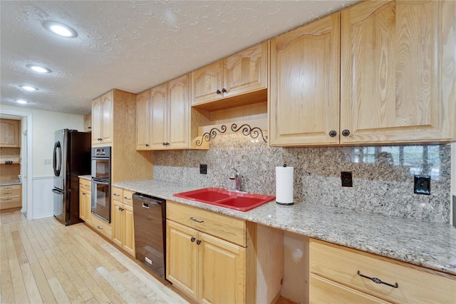 kitchen with light brown cabinetry, light wood-style floors, a sink, a textured ceiling, and black appliances