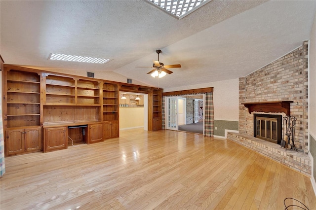 unfurnished living room with a textured ceiling, light wood-style flooring, a fireplace, vaulted ceiling, and built in study area