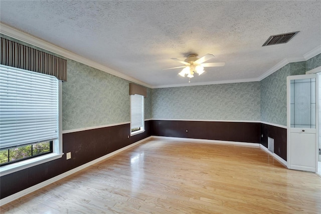 empty room featuring a textured ceiling, wainscoting, visible vents, and wallpapered walls