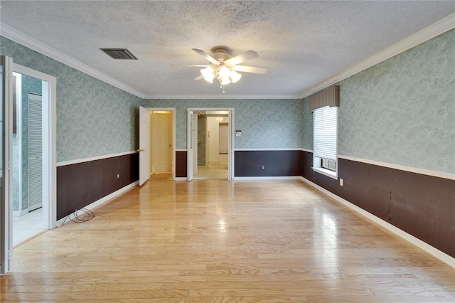 spare room featuring visible vents, a wainscoted wall, a textured ceiling, and wallpapered walls