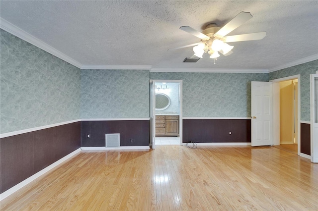 interior space with wallpapered walls, visible vents, a textured ceiling, and wainscoting