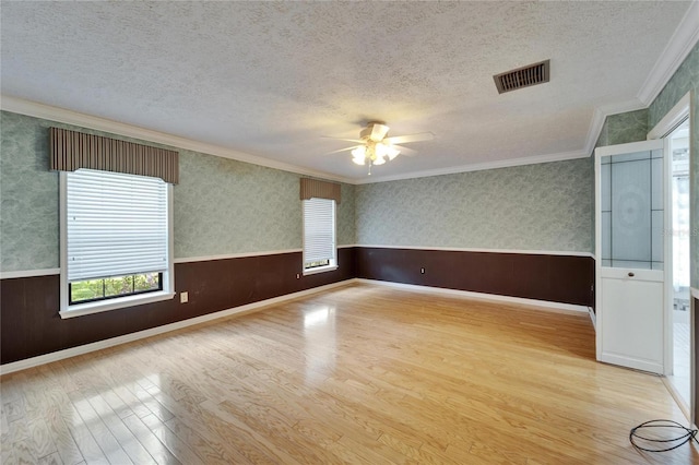 spare room with wainscoting, visible vents, a textured ceiling, and wallpapered walls