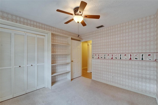 unfurnished bedroom featuring wallpapered walls, visible vents, carpet, a textured ceiling, and a closet