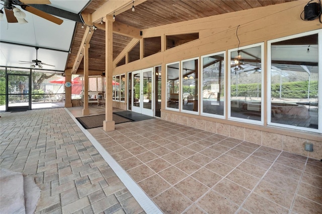 unfurnished sunroom featuring vaulted ceiling with beams, wooden ceiling, ceiling fan, and a healthy amount of sunlight