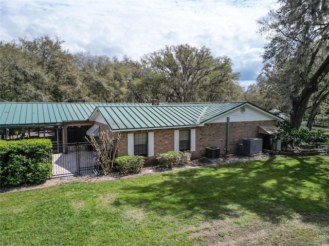 rear view of property with a lawn, metal roof, a standing seam roof, cooling unit, and brick siding