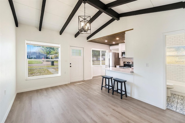 679 71st Ave N, Saint Petersburg, FL 33702 - kitchen with lofted ceiling with beams, backsplash, appliances with stainless steel finishes, white cabinets, and a chandelier
