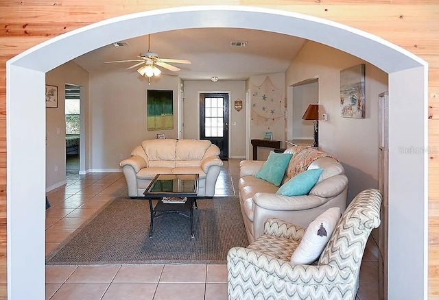 tiled living room featuring arched walkways, baseboards, visible vents, and a ceiling fan