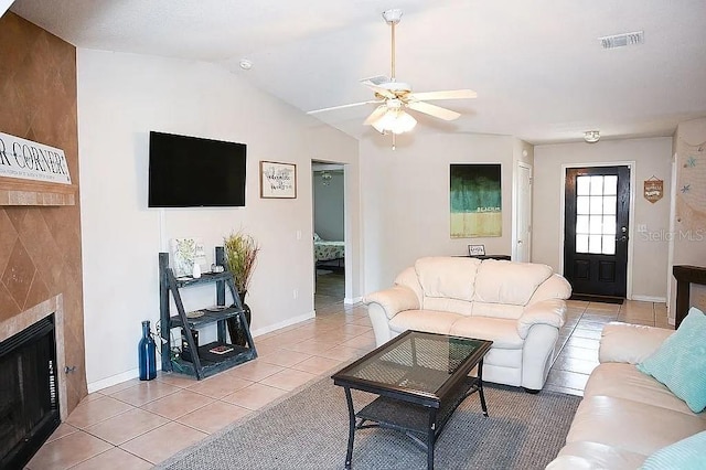 living area with light tile patterned floors, lofted ceiling, a fireplace, visible vents, and a ceiling fan