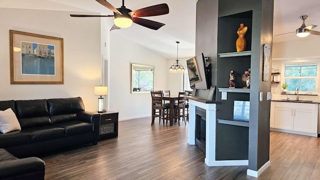 living area featuring a fireplace, dark wood finished floors, lofted ceiling, baseboards, and ceiling fan with notable chandelier