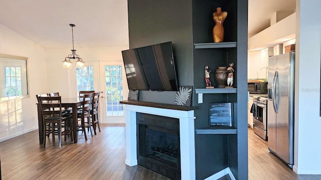 kitchen featuring lofted ceiling, a fireplace, wood finished floors, appliances with stainless steel finishes, and pendant lighting