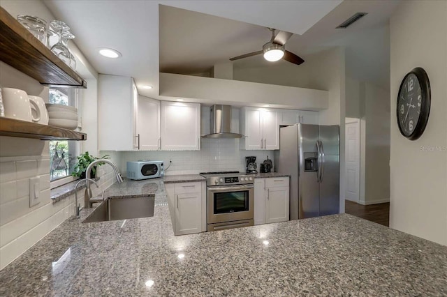 kitchen with stone counters, a sink, wall chimney range hood, appliances with stainless steel finishes, and decorative backsplash