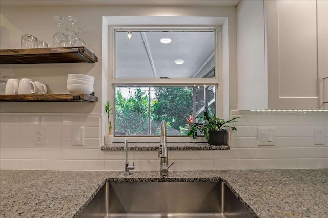 kitchen with open shelves, backsplash, a sink, and light stone countertops