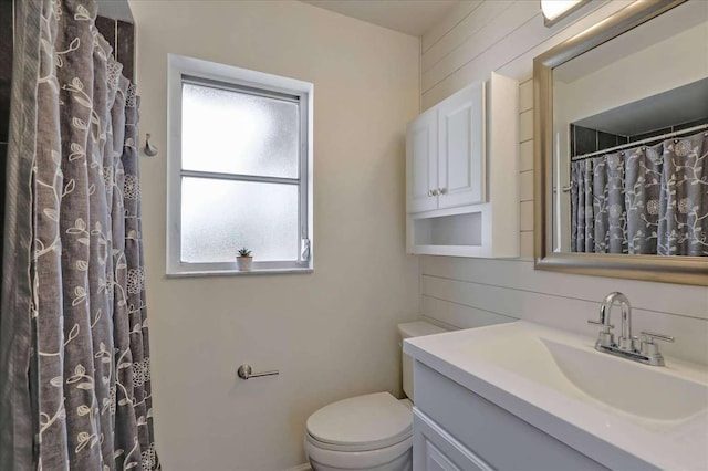 bathroom featuring toilet, curtained shower, wooden walls, and vanity