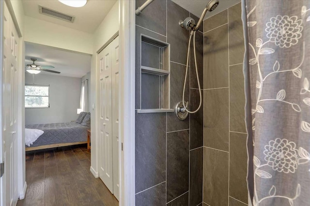 bathroom featuring a ceiling fan, wood finished floors, visible vents, and tiled shower